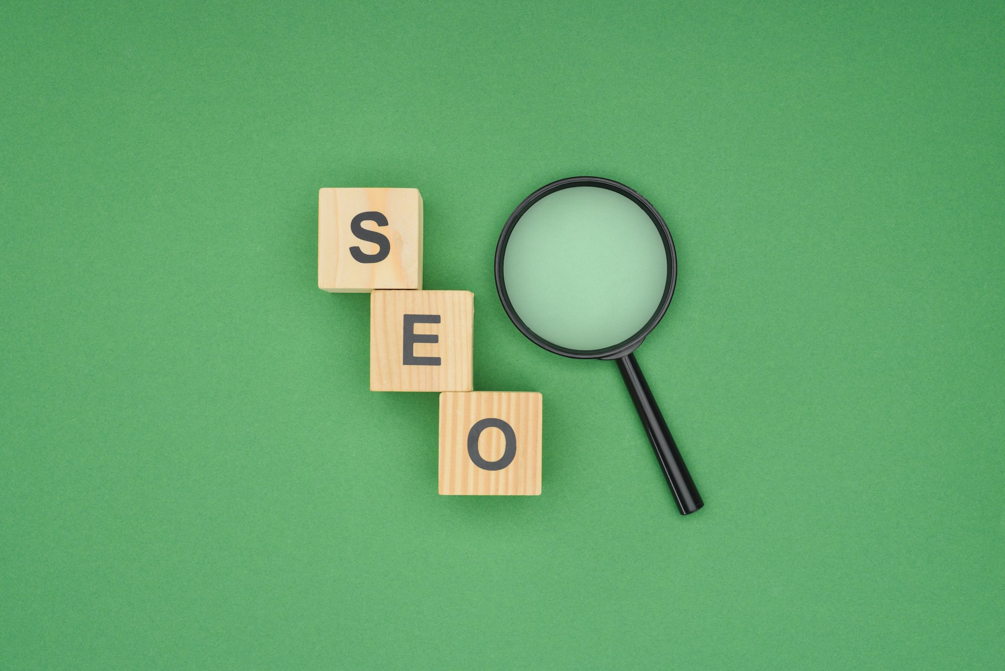 Top view of wooden cubes with seo lettering and magnifier glass on green background